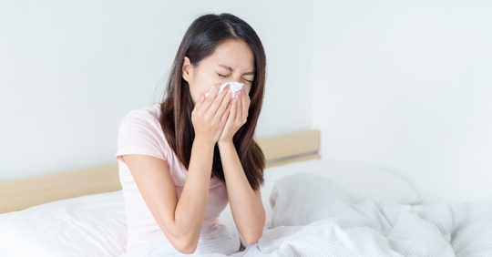woman sneezing in bed